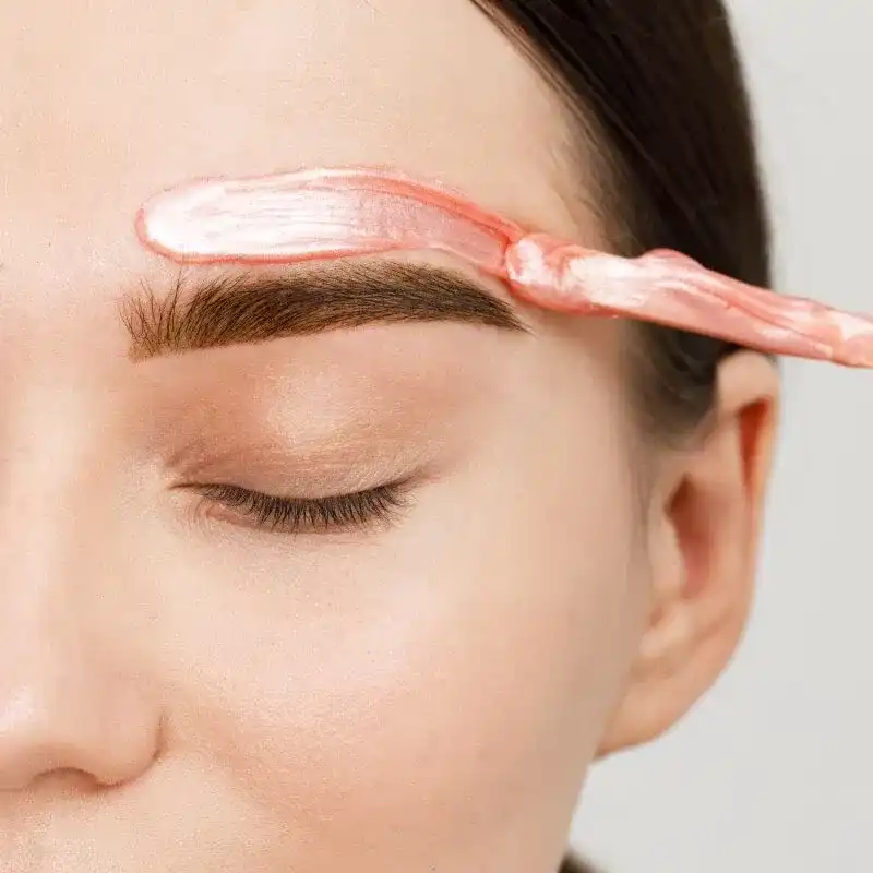 Eyebrow being waxed with pink wax, close-up on a woman's face.