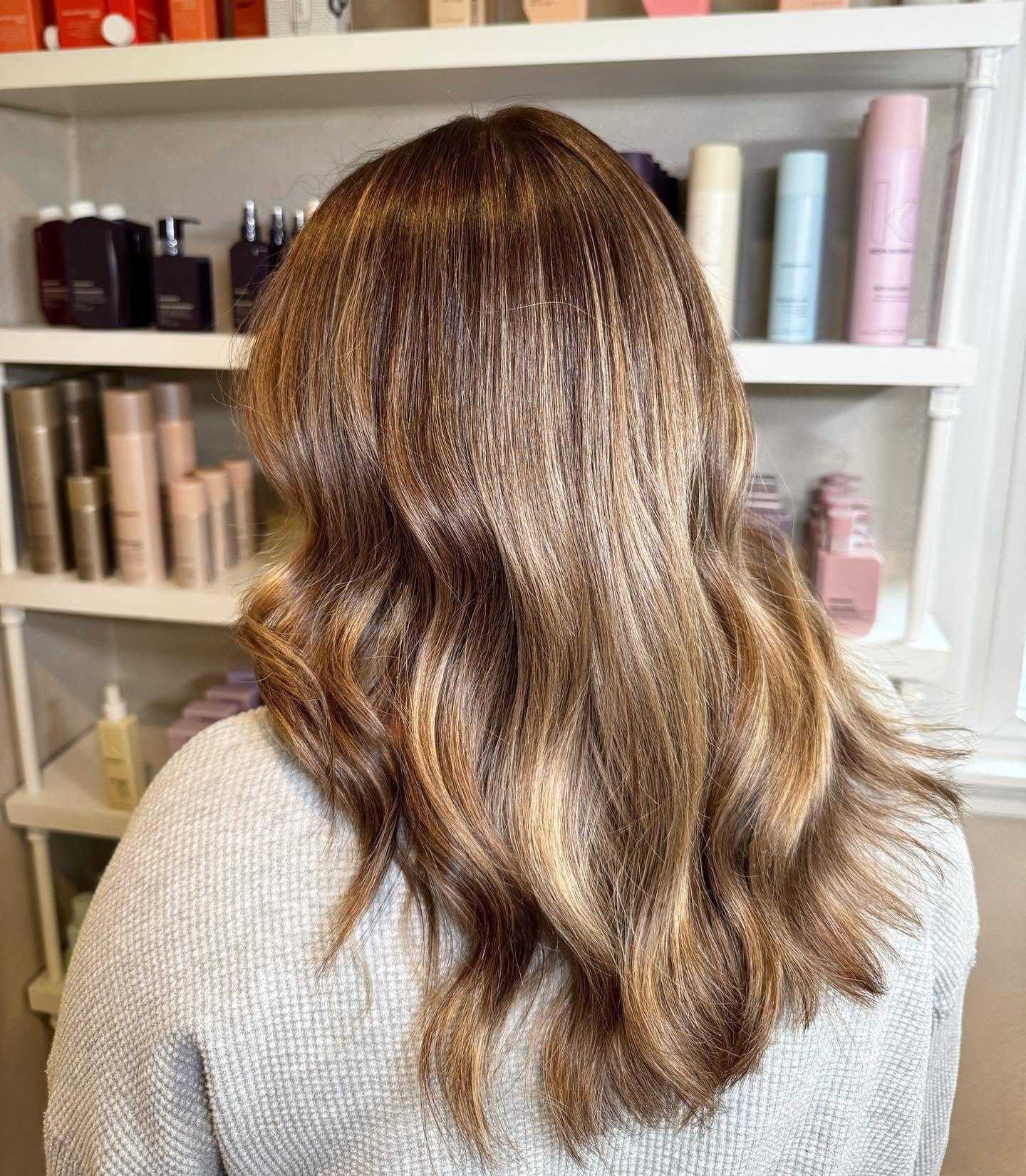 Wavy, light brown hair with blonde highlights in a salon setting.