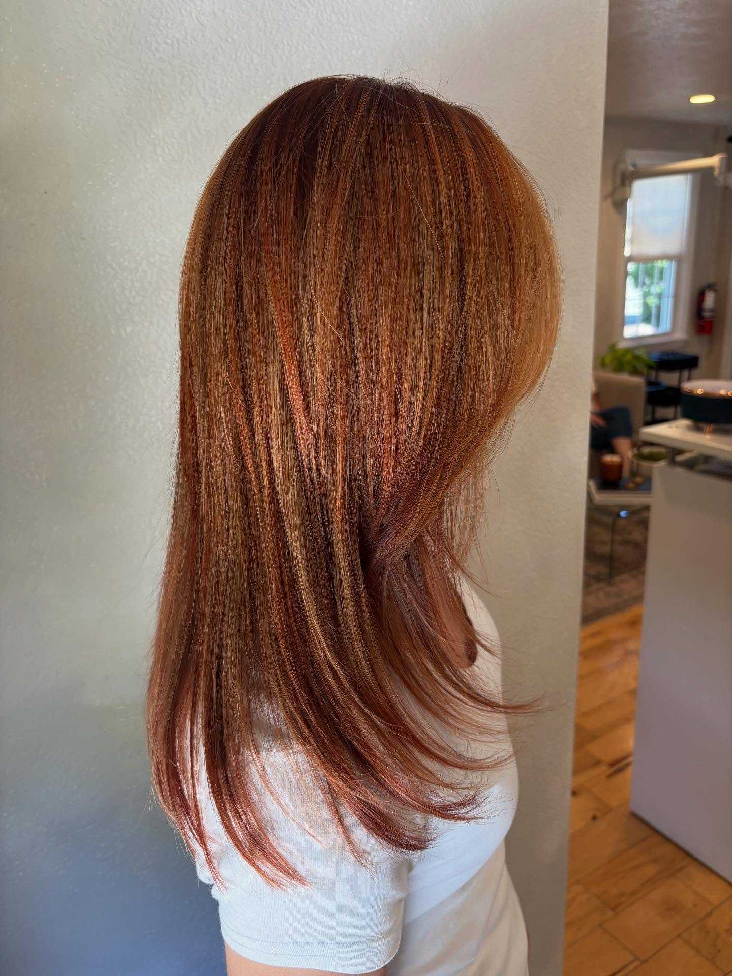 Red-toned layered hairstyle on person with straight hair in indoor setting.