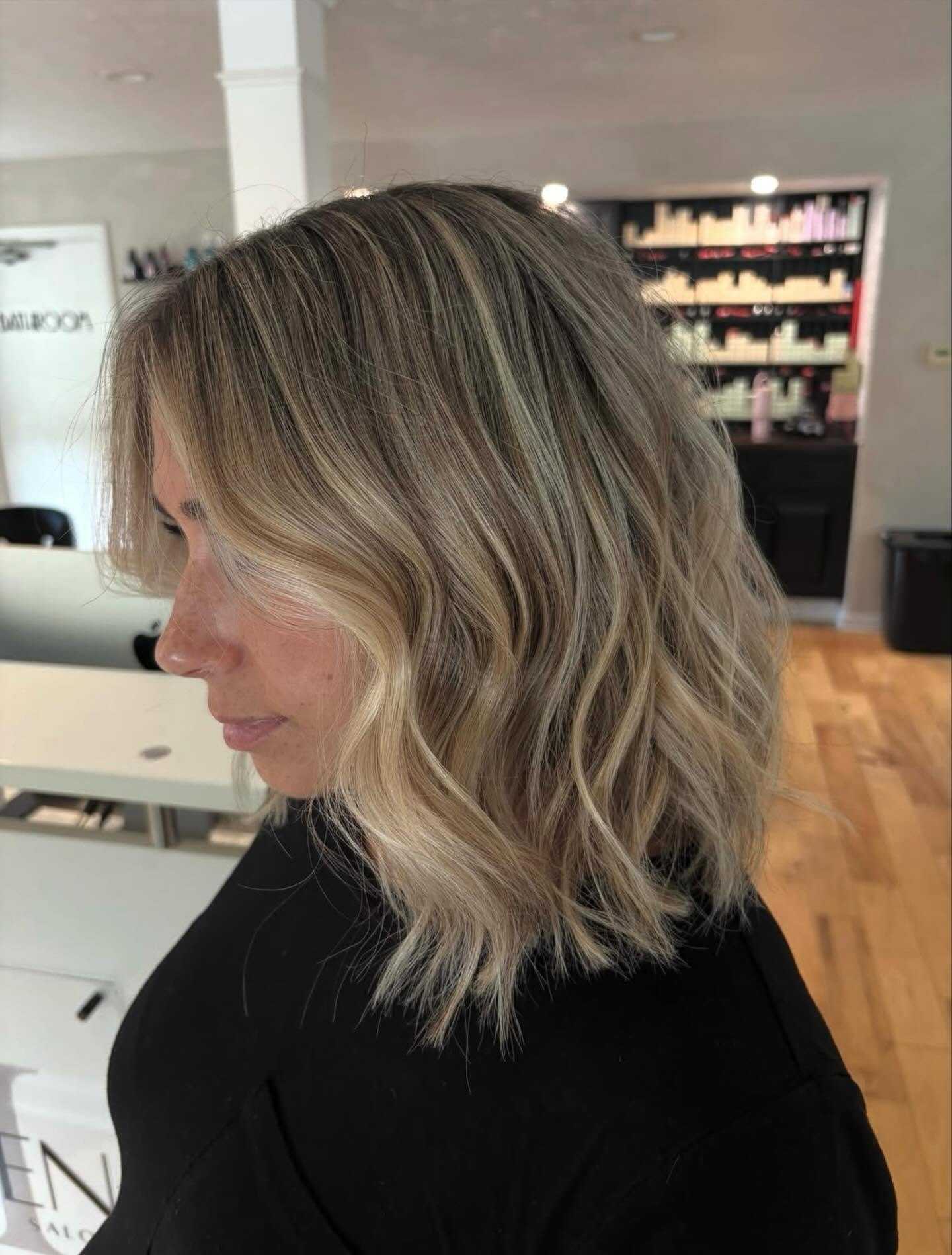 Blonde woman with wavy, shoulder-length hair at a salon with haircare products in the background.