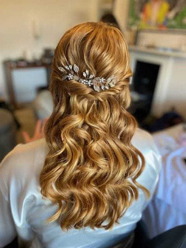 Golden curls cascading with floral hair accessory in elegant bridal hairstyle.